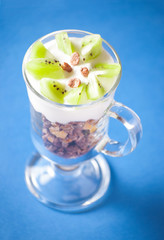 Muesli yogurt and kiwi in glass on blue background