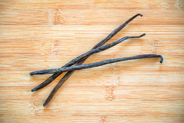 Three vanilla pods with a flower on wooden background