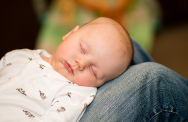 A baby sleeps comfortably on his father's lap