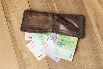 brown leather wallet with money on wood board background