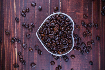 roasted coffee beans in white heart bowl porcelain on wooden bac