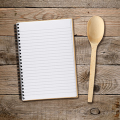 Recipe book and spoon on wooden background