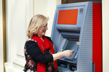 Mature blonde woman with credit card in hand near ATM