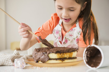 Mixed race girl icing cake in kitchen