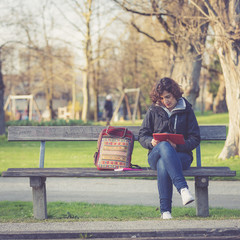 young girl sitting on a bench at park and reading E-book