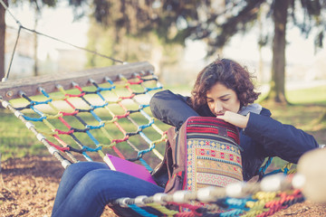 Young student sitting in hammock and searching in her backpack