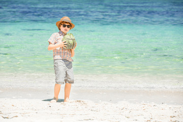 Happy young boy staying on beautiful ocean beach wearing hat and
