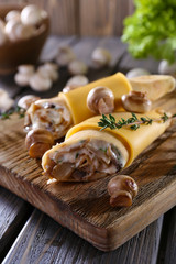 Pancakes with creamy mushrooms on cutting board on wooden table, closeup
