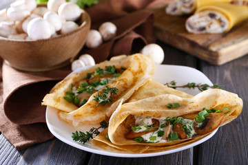 Pancakes with creamy mushrooms in plate on wooden table, closeup