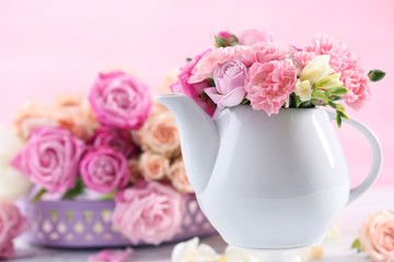 Composition with beautiful spring flowers in teapot on light pink background
