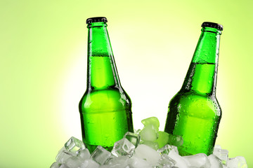 Glass bottles of beer in ice cubes on color background