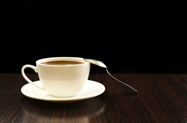 Cup of coffee on wooden table, on dark background