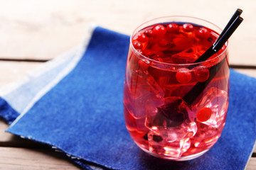 Glass of compote with red currant on wooden table with jeans cloth, closeup
