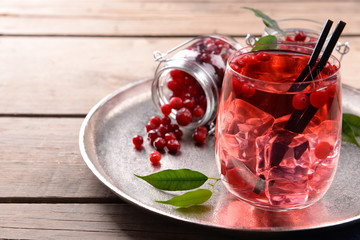 Compote with red currant in glassware on metal tray on wooden table, closeup