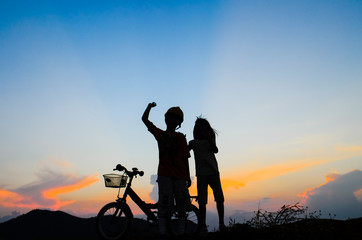 Obraz premium Boy with his sister riding bicycle on sunset background.Silhouet