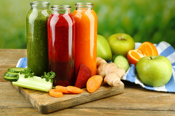 Assortment of healthy fresh juices in glass bottles on wooden table, on bright background