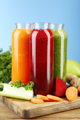 Assortment of healthy fresh juices in glass bottles on wooden table, on blue background