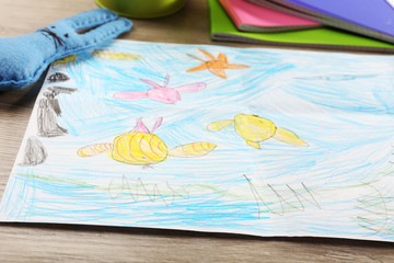 Kids drawing on white sheet of paper on wooden table, closeup