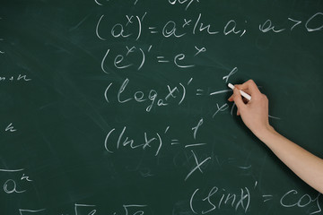 Female hand writing formulas on blackboard with chalk, close up