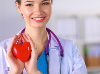 Young woman doctor holding a red heart, standing in hospital