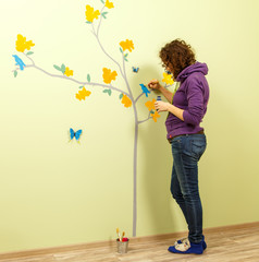 Female artist draws tree, butterflies and birds on the wall