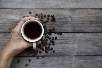 Female hands holding cup with coffee beans on wooden table backg