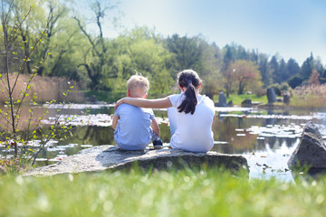 Dzieci siedzą na brzegu jeziora  - obrazy, fototapety, plakaty