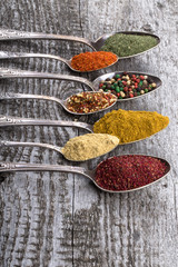 Antic metal spoons with different kinds of spices on old wooden