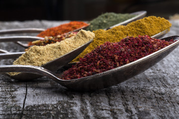 Antic metal spoons with different kinds of spices on old wooden