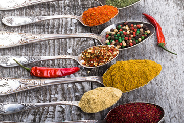 Antic metal spoons with different kinds of spices on old wooden