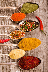 Antic metal spoons with different kinds of spices on old wooden