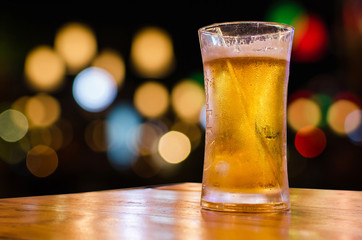 Glass of beer with bokeh bar scene in the background.