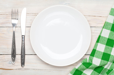 Empty plate, silverware and towel over wooden table background