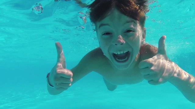Cute teen boy dives in blue pool with open eyes
