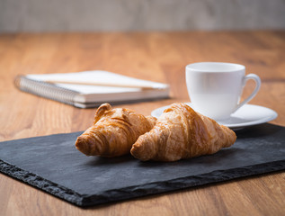 Two tasty french croissants with a cup of coffee and notebook