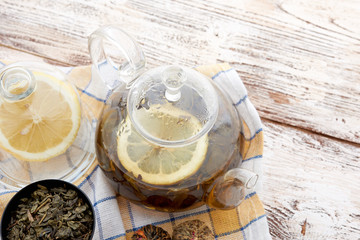 Ripe lemon, cinnamon and fruit drink in glass teapot on wooden