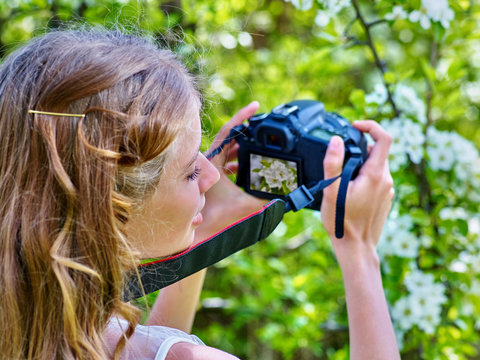 Girl photographs blossoming tree.
