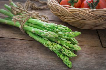 Bunch of asparagus on wooden table and tomato in basket