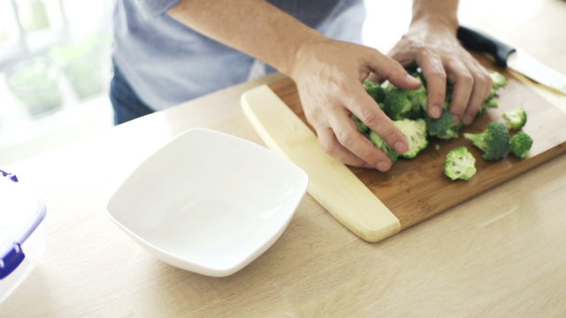 Man putting broccoli into bowl in kitchen
