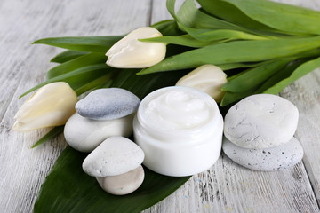 Cosmetic cream with flowers and spa stones on wooden background