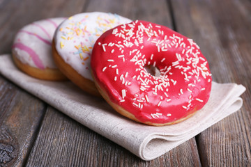 Delicious donuts with icing on napkin on wooden background
