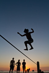 Silhouette of young man balancing on slackline at a beach in