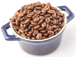 Roasted coffee beans in a blue ceramic pot over white background