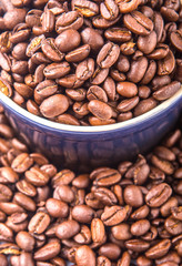 Roasted coffee beans in a blue ceramic pot over white background