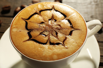 Cup of coffee latte art with grains on wooden table, closeup