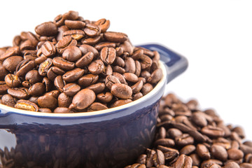Roasted coffee beans in a blue ceramic pot over white background