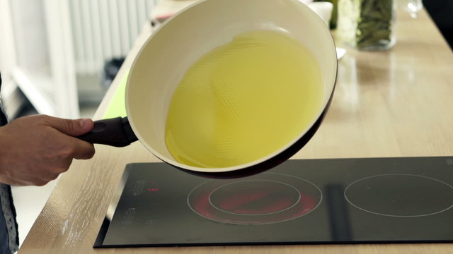 Man hand spreading olive oil on pan over induction 
