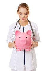 Young female doctor holding a piggybank.