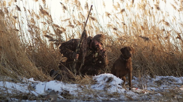 hunter and his dog on the snowy bank of a pond duck hunting