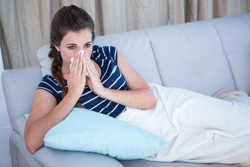 Sick woman blowing her nose on couch